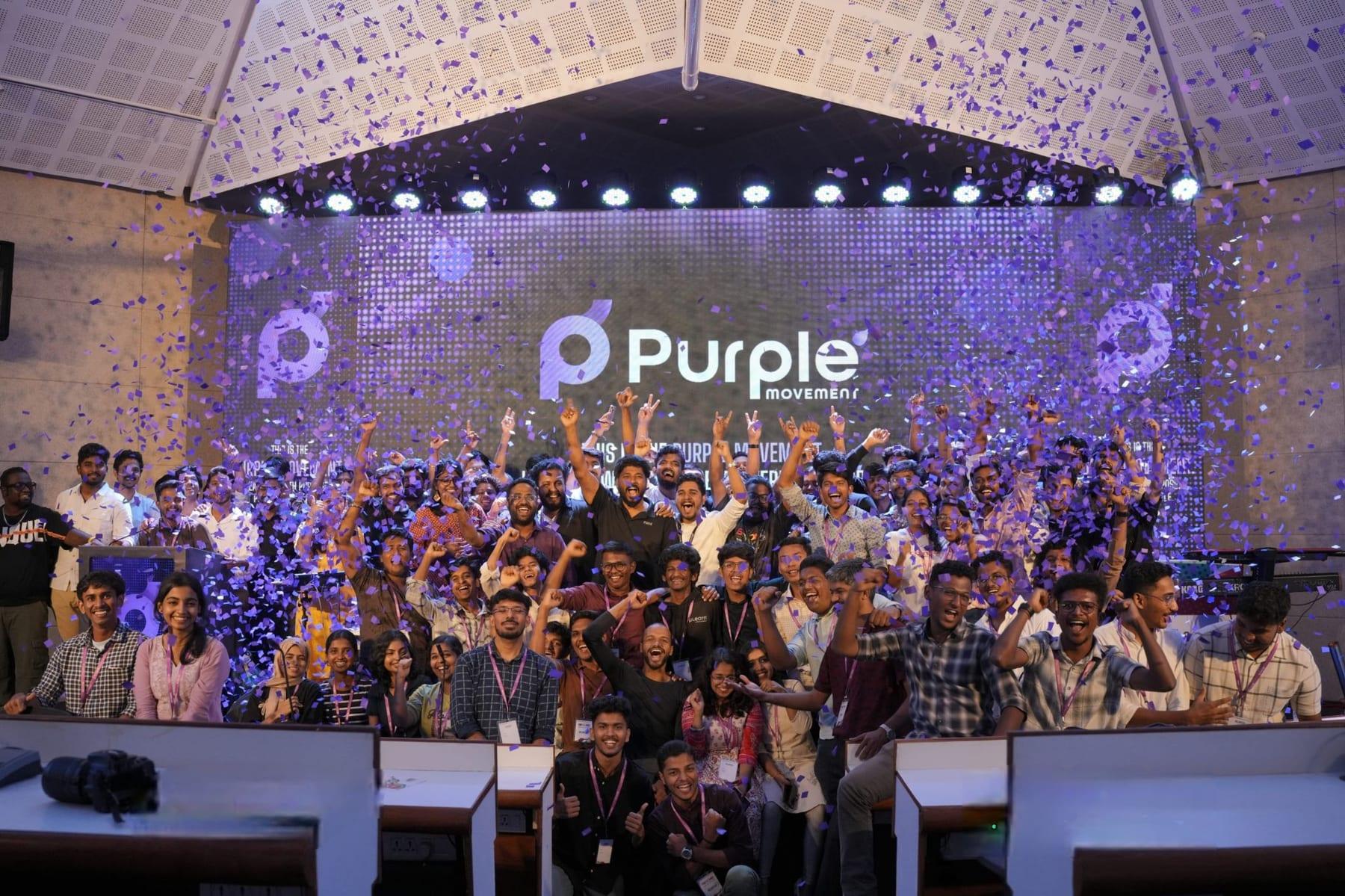 A large group of young people and professionals cheer on stage under falling purple confetti in front of a screen reading Purple Movement.